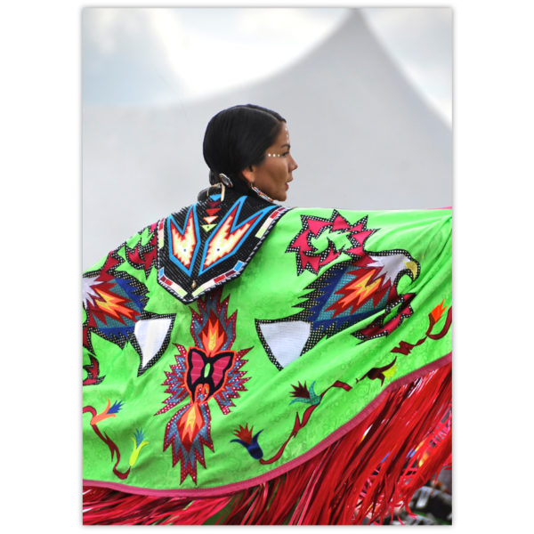 a beautiful aboriginal woman dances at a Canadian Pow Wow. Her regalia is a vibrant green background with a long red finge and intricate designs including an eagle motif