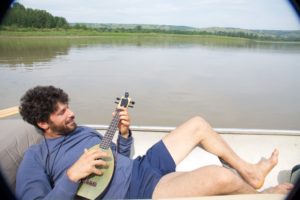 Tree planter playing a ukulele while floating down the river